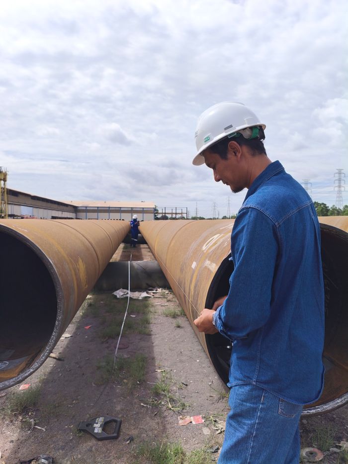 Engineers in helmets inspect large pipelines at an outdoor construction site.